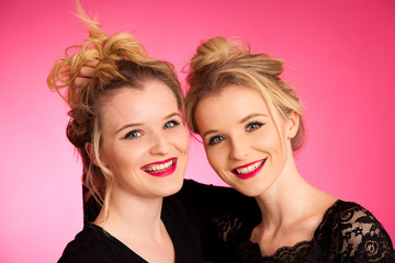 Portrait of twin sisters over pink background