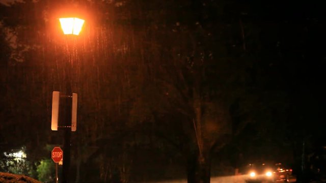 A nighttime rainstorm creates a reddish glow from the streetlight and passing vehicles.