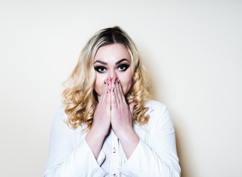 Blonde woman on a light background covered her mouth with her hands in surprise