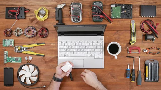 Male engineer programmer copies files from a flash card action camera on a laptop. Wooden table top view. Uses cardreader