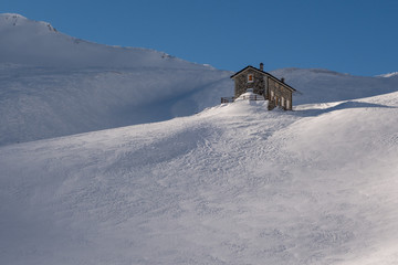 Alpine refuge below mountain ridge in winter on windswept snow u