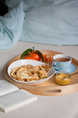 Gemütliches Frühstück im Bett serviert auf einem Tablet, mit Pfannkuchen im Teller, Lemon Curd in Glasschale und Tee oder Kaffee in der Tasse, frisches Obst