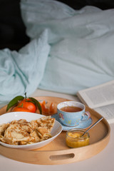 Gemütliches Frühstück im Bett serviert auf einem Tablet, mit Pfannkuchen im Teller, Lemon Curd in Glasschale und Tee oder Kaffee in der Tasse, frisches Obst