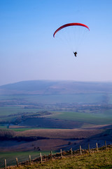  paraglider in the sky, with red canapy, ladscape of fields belo