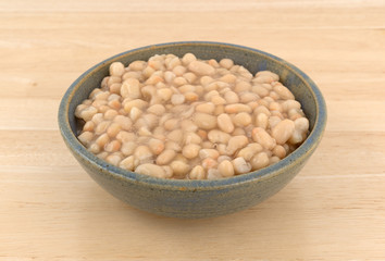 Organic navy beans in a stoneware bowl atop a wood table. 