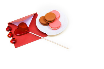 Open red envelope, lollipop in the shape of a heart and macarons on the white background.