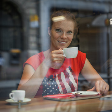 Young woman drinking cappuccino coffee in a shop window in a Par
