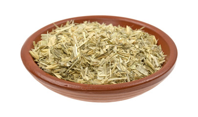 Bowl of dried and shredded oatstraw herb isolated on a white background.