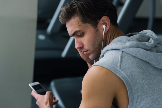 Handsome Young Man In Headphones Using His Smart Phone  At Gym