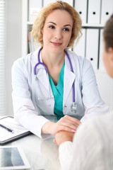 Happy blonde female doctor looking at  patient while speaking to her and reassuring. Medicine, healthcare and help concept