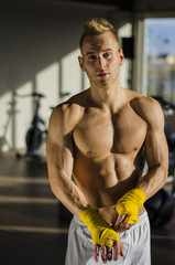 Obraz premium Muscular young man wrapping bandage around his hands for boxing