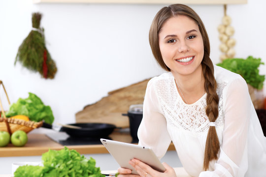 Young  woman is making online shopping by tablet computer. Housewife looking for a new recipe for  cooking in a kitchen