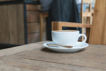 White cup of coffee on wooden table in the coffee shop.