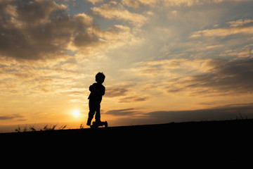 silhouette of a boy,little boy riding scooter at sunset time