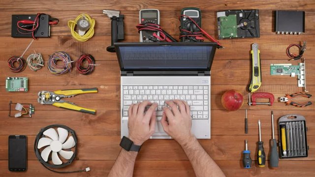 Male engineer prints for the laptop and check the messages on the smart watch. Wooden table top view