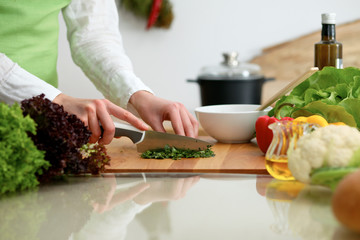 Closeup of human hands cooking vegetables salad in kitchen on the glass table with reflection. Healthy meal and vegetarian concept