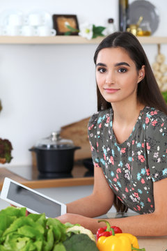 Young hispanic  woman is making online shopping by tablet computer and credit card. Housewife found new recipe for  cooking in a kitchen