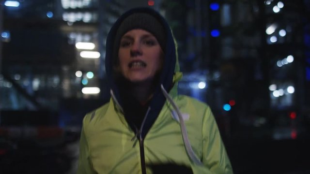 4K Female jogger in hi vis jacket running in the city at night, in slow motion