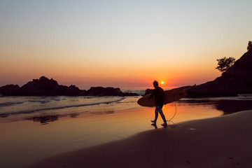 Fototapeta na wymiar Surfer walking on the beach to the water at sunrise