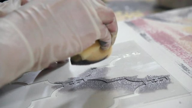 Hands of professional craftsmen decorate the paper using paint and a stencil. Creative process in a professional design studio. Slow motion.