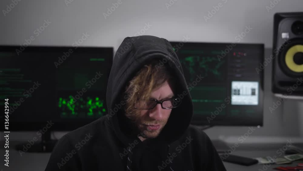 Poster close up of a spy with smartwatch sitting and using laptop with computer monitors behind him. crimin
