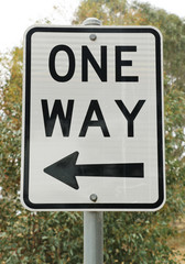 black and white one way sign against a tree background
