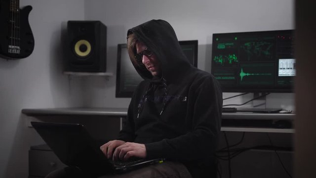 A hacker is preparing for cyber-attack in the underground computer room. A man at a rapid pace enters the information on his laptop. On monitors the information on the preparations for hacker attack.