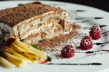 Tiramisu cake with cognac and raspberries on a white dish