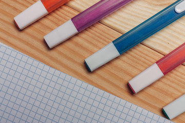 multicolored markers and a sheet in a cage on a wooden background