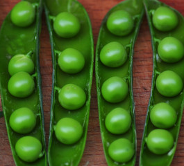 Open green peas in pods on wooden board