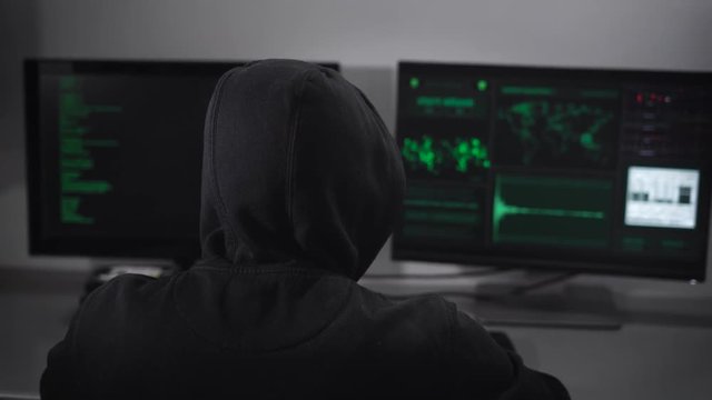 Rear view on the hacker who is engaged clandestine cyber attacks to the server with the data bank. Culprit in the IT field gets illegally accessing funds on the Internet.
