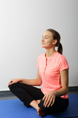 Fototapeta premium Yoga smiling girl sitting with legs crossed, her hands on feets.