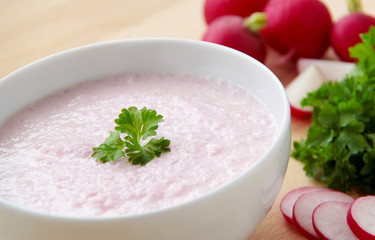 Vegetable spring radish soup. Bowl of radish soup surrounded by ingredients. Wooden background. Closeup view.