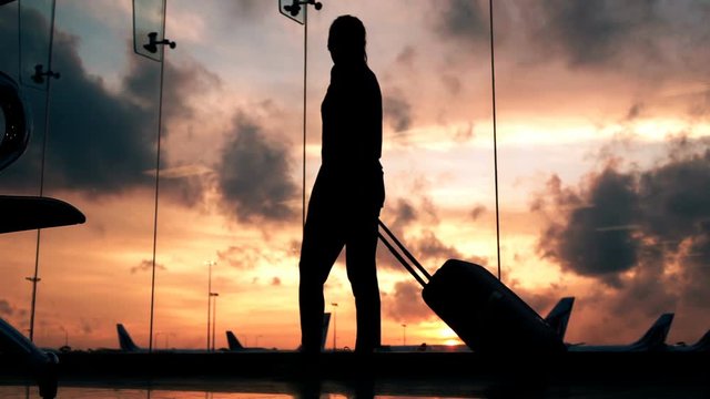 Silhouette of woman with suitcase walking through hall at airport, super slow motion 240fps
