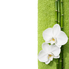 Three orchids and white terry towel  lying on shabby wooden board.  Viewed from above. Spa concept.