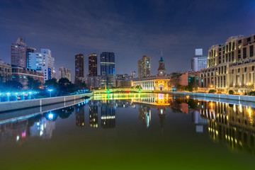 River And Modern Buildings Against Sky at night.