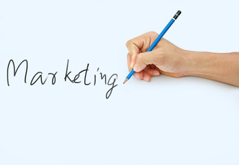 Hand holding a pencil on a white paper background, writing with pencil for word " Marketing "
