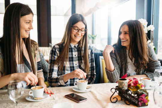 Three smiling women enjoy coffee talk at cafe