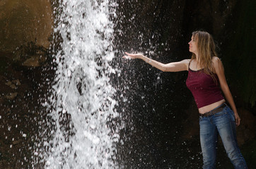 Wet woman put her hand in waterfall's water and enjoying
