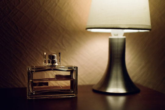 Table top lamp with burlap shade lit on a wooden table and a bottle of male perfume.