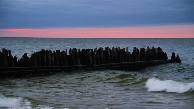 The sun sets on Lake Superior as waves break around an old wooden groyne positioned to halt beach erosion at Michigan's Crisp Point Lighthouse. Seamless 60 second loop.