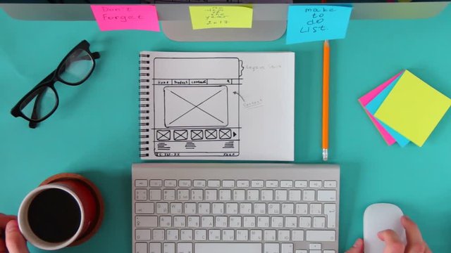 Top view of blue workbench wizard which is web sketch. Man scrolling the mouse and drink coffee.