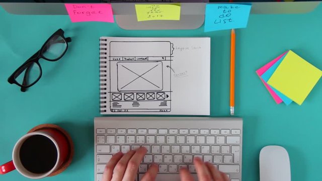 Top view of working place in the blue table. The web master is working on the computer, making the site layout drawn on the sketch.