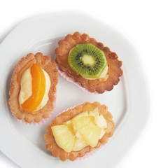 Tortine alla crema e frutta su piatto su sfondo bianco