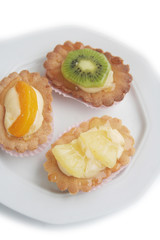 Tortine alla crema e frutta su piatto su sfondo bianco