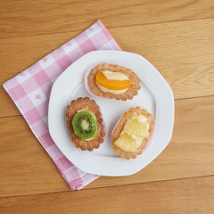 Tortine alla crema e frutta su piatto su tavolo di legno