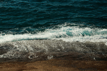 Beautiful aquamarine sea waves crash against brown stones