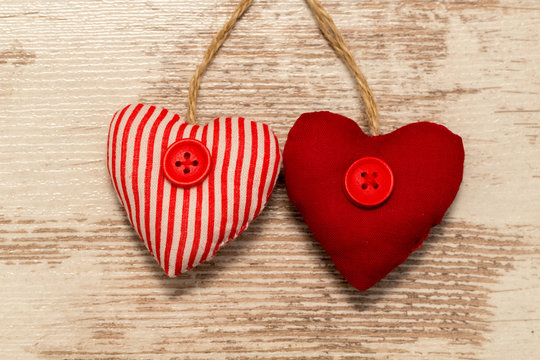 2 rote Herzen aus Stoff hängend vor hellem Holz
