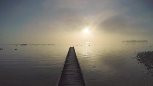 POV shot of walking on a wooden jetty over lake chiemsee, bavaria, germany against misty sky during sunrise