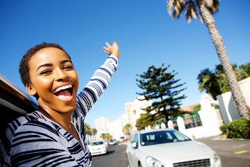 young woman hanging outside car window with arms raised